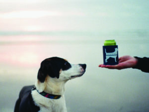 a dog inspects a blue koozie that features a dog illustration