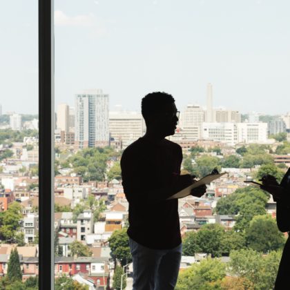 coworkers stand and talk in front of a large window overlooking a city