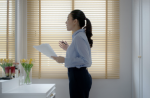 young female asian woman happy stands in front of mirror holding sheet of paper practicing speech