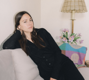 Tasha Young, a copywriter and content writer, sit on a white couch in all black.